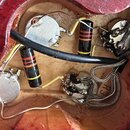 Fotografie zachycuje vnitřek elektroniky v červeném dřevěném korpusu nástroje. Jsou zde vidět čtyři kovové potenciometry, tři válcové kondenzátory s…