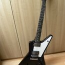 Černá elektrická kytara s bílým pickguardem v tvaru V. Na hlavě hmatníku je bílý nápis BYCH. Nástroj má dva humbuckery, jeden potenciometr a přepínač…