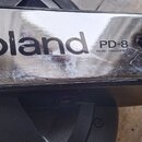 Detail kovového a plastového dílu s nápisem Roland PD-8 DUAL TRIGGER PAD. Povrch kovové části je výrazně poškrábaný a vykazuje známky opotřebení. V p…