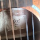 Fotografie zachycuje vnitřek akustické kytary s viditelným štítkem uvnitř korpusu. Na štítku je uveden nápis Cort GUITARS, MODEL: AF510M OP a SERIAL…
