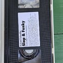 Černá videokazeta v bílém plastovém obalu. Na štítku je uveden text: „Richard Scheufler Slap & Funky Kreativní škola hry na basovou kytaru“. Jsou zde…