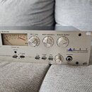Stříbrný rackový mikrofonní předzesilovač s nápisem ART APPLIED RESEARCH AND TECHNOLOGY. Na předním panelu jsou dva VU metry, tři otočné oválné knofí…