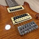 Detail elektrické kytary s tělem z plamenového javoru v hnědém odstínu. Nástroj má dva humbuckery s krémovými rámečky a jeden ovládací knoflík v mědě…