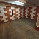 Fotografie zachycuje interiér místnosti s betonovou podlahou. Stěny jsou vyloženy akustickými panely v červenohnědé a bílé barvě, uspořádanými do šac…