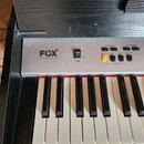 Digitální klavír v černém dřevěném korpusu se stříbrným ovládacím panelem. Na panelu je nápis FOX KEYBOARDS, vypínač POWER a řada ovládacích tlačítek…