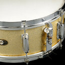 Detailní pohled na zlatý buben s glitrovým povrchem a chromovanými obručemi. Na korpusu je oválný štítek s nápisy „Slingerland“, „QUALITY DRUMS“ a „C…