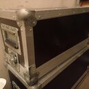 Na fotografii jsou dva černé transportní kufry s hliníkovými hranami a kovovými rohy. Horní kufr má na čelní straně kovovou rukojeť a zámek. Povrch h…