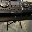 Černý DJ 컨트롤러 s dvěma jogovými koly a centrálním displejem. Na přístroji jsou viditelné nápisy Numark, MIXSTREAM PRO a engine os. Zařízení je umístěn…