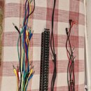 Sada kabelů a rozbočovací panel v černé barvě. Panel obsahuje řadu vstupů a výstupů, z nichž některé jsou zapojeny do černých kabelů s konektory typu…