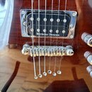 Detail elektrické kytary v tmavě hnědé barvě s viditelnou strukturou dřeva. Je zde zobrazen chromovaný snímač s nápisem Seymour Duncan a chromovaný k…