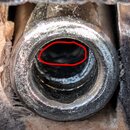 Detailní záběr na kovový vstupní konektor, pravděpodobně jack socket. Povrch kovu vykazuje známky opotřebení, oxidace a nečistoty. Horní část otvoru…