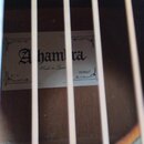 Detail pohledu do korpusu akustické kytary. Uvnitř je nalepený bílý štítek s nápisy „Alhambra“, „Made in Spain“, „S1C“ a „MCBQcT“. Povrch dřeva v oko…