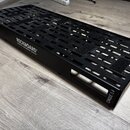 Černý kovový pedalboard s perforovaným povrchem a bočními úchopy. Na boku je bílý nápis ROCKBOARD by WARWICK a v pravém dolním rohu označení CINQUE 5…