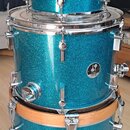 Tři modré glitrové bubny v různých velikostech naskládané na sebe. Každý buben má na korpusu oválný štítek s nápisem „Zildjian MARTIN“. Kovové obruče…