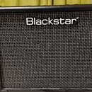 Černý kytarový kombo zesilovač s texturovaným povrchem a mřížkou reproduktoru. V horní části je bílý nápis Blackstar. Nástroj vykazuje mírné opotřebe…