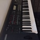 Černý digitální klavír s bílými a černými klávesami. Na levé straně je bílý nápis YAMAHA a vedle něj logo značky. Ovládací panel obsahuje displej, ně…