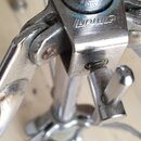 Detail chromovaného kovového stojanu s utahovacím šroubem. Na horní části je vyryt nápis "Sonor". Povrch vykazuje známky opotřebení, oxidaci a drobné…
