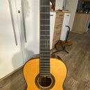 Kytara s vyřezem (cutaway), přírodní dřevěná barva těla a tmavý hmatník. Na hlavě nástroje jsou vidět zlaté ladičky, žádné značky ani názvy modelů ne…