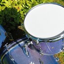 Tři bubny v modré barvě s kovovými obručemi a mechanismy. Na bílém blaně pravého bubnu je nápis „Evans ECCORE HEAD MADE IN USA“. Na korpusu levého bu…