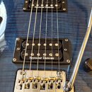 Detail modré kytary s viditelnou strukturou dřeva. Na instrumentu jsou dva černé snímače s bílým nápisem Seymour Duncan a chromovaný kobylník. V horn…