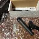Na fotografii je černý dynamický mikrofon, držák na mikrofon a originální krabice s nápisy SHURE SM57 Legendary Instrument Microphone. Mikrofon leží…