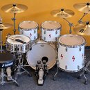 Bílá bubnová sada s červenými symboly blesků na korusech. Na basovém bubnu je nápis REMO a na čínalech značky Istanbul Agop, Xist a Meinl Classic. Sa…