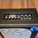 Černý kytarový kombo zesilovač s bílou mřížkou reproduktoru. Na přední straně je nápis MCGEE HARLEY a ovládací panel s knoflíky označenými MOD, DELAY…