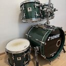 Sada bubnů v tmavě zelené barvě s chromovaným hardwarem. Na basovém bubnu je bílé logo SONOR a nápis DRUMCENTER.CZ, na ostatních bubnech jsou viditel…