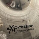 Detail stříbrného činchimu s koncentrickými rýhami na povrchu. Na nástroji je černý nápis expression a pod ním text 13"/33cm Regular Hi-Hat Bottom. P…