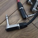 Fotografie zobrazuje tři kabelové konektory typu jack s úhlem 90 stupňů. Konektory mají stříbrné kovové části a černé plastové kryty s vrubcovaným pr…
