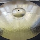 Kovový činel zlatavé barvy s koncentrickým žebrováním povrchu. Na povrchu jsou čitelné nápisy „Paiste“ a „Power Crash 18"“. Povrch je čistý a bez vid…