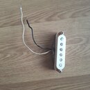 Bílý snímač typu single-coil s pěti viditelnými magnetickými póly. K snímači vedou dva volné vodiče, jeden bílý a jeden černý. Snímač je upevněn dvěm…