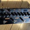 Černý kytarový efektový pedál s oranžovými nápisy DELAY, MOD, DIST a DRIVE. Na přístroji jsou viditelné značky Cerberus a NUX, dále nápisy GLOBAL, RO…