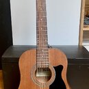 Akustická kytara s hnědým trupem, vyřezem v těle a tmavým hmatníkem. Na hlavě je zlatý nápis Ibanez. Uvnitř otvoru kytary je viditelný štítek s nápis…
