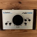 Stříbrný monitorovací kontroler s černými bočními kryty. Na horní části je nápis M-Control + PASSIVE MONITOR CONTROLLER a logo swissonic. Zařízení ob…