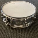 Kovový snare drum s chromovaným povrchem a bílou blánou. Na bláně je viditelné logo REMO. Na korpusu se nachází oválný štítek s nápisem DYNA-SONIC CU…