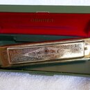 Stříbrná harmonika v zeleném plastovém pouzdře s červeným vnitřním polstřením. Na víčku nástroje je vyryt ornament a nápisy TRADE MARK, M.HOHNER, GER…