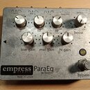 Kytarový efekt pedál v kovovém šasi stříbrné barvy. Na spodní části je černý štítek s nápisy „empress effects ParaEq w/Boost“ a pod ním text „Made in…