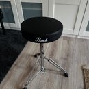 Černý polstrovaný bubeníckýstolek s chromovaným třínohým stativem. Na boku sedáku je bílý nápis Pearl. Povrch sedáka i chromované části vypadají čist…