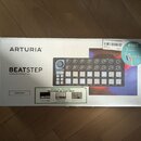 Fotografie znázorňuje papírovou krabici od hudebního zařízení. Na krabici je nápis ARTURIA a BEATSTEP Controller & Sequencer spolu s obrázkem černého…