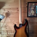 Zadní strana elektrické kytary s trupem v barevném přechodu od černé přes červenou k žluté (sunburst) a světlým dřevěným hnedem krku. Na spojení krku…