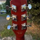 Zadní strana hlavy kytary v červenohnatém lakovaném provedení. Jsou zde vidět šest chromovaných ladiček. Dole na hlavě je nápis Designed and Backed b…