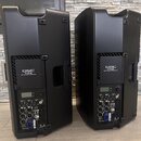 Dvě černé aktivní reprodukce z plastu v podobě kompaktních beden. Na zadním panelu každého reproduktoru je nápis QSC K12.2 2KW 12" ACTIVE LOUDSPEAKER…