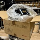 V kartonové krabici s nápisem SNARE DRUM a logem TAMA je umístěn černý malý buben zabalený v průhledné plastové fólii. Na korpusu nástroje je viditel…
