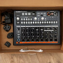 V kartonové krabici leží černý bicí automat s nápisem DRUMBRUTE IMPACT a podtitulem BEAT SMASH DRUM MACHINE. Zařízení má ovládací panely s různými kn…