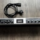 Stříbrné rackové zařízení s černým předním panelem a nápisem ULTRAGAIN PRO. Na pravé straně je logo a značka behringer oraz vypínač POWER. Přístroj o…