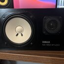 Černý studiový monitor s bílým membránovým reproduktorem a menším výškovem krytým kovovou mřížkou. Na pravém spodním rohu je bílý nápis YAMAHA a pod…