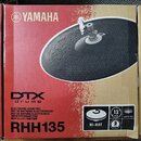 Kartonová krabice s červeným a bílým potiskem. Na krabici je zobrazen černý elektronický činel a nápisy YAMAHA, DTX drums, RHH135 a ELECTRONIC DRUM P…