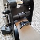 Detailní pohled na černý kovový mechanismus bicího pedálu. Je vidět pružina, kloubové spojení a kovová šlapka s černou gumovou vložkou. Na součástích…