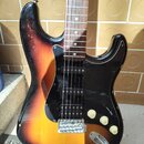 Elektrická kytara s trupem v barevnosti sunburst a černým pickguardem. Nástroj má tři snímače, tři bílé ovládací knofíky a chromovaný most s páčkou.…